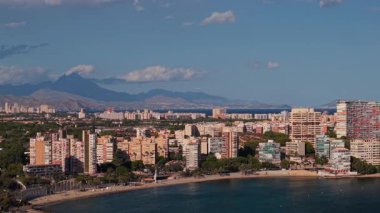 Alicante sahil şeridi, Albufereta plajı, yerleşim binaları ve açık mavi gökyüzünün altındaki dağlar. Yüksek kalite 4k görüntü