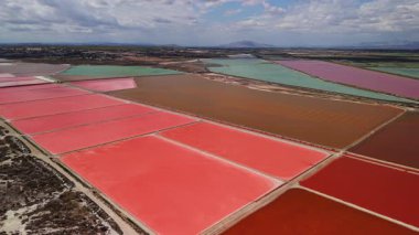 Santa Pola, Alicante, İspanya yakınlarındaki renkli tuz buharlaştırma göletlerinin havadan görünüşü. Canlı kırmızı, pembe, yeşil ve kahverengi tuz düzlükleri soyut desenler oluşturuyor. Yüksek kalite 4k görüntü