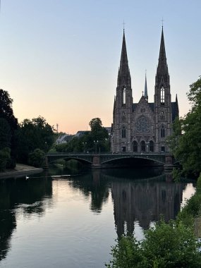 Saint-Paul Kilisesi ve Pont d 'Auvergne köprüsü Strasbourg, Grand Est, Fransa, Haziran 2023' te gün batımında L 'll nehrine yansıdı.