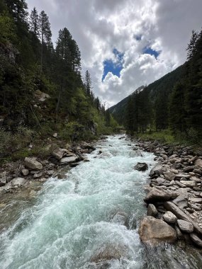 Dağ nehri Krimmler Ache Krimmmml, Salzburg, Avusturya, Mayıs 2024 yakınlarındaki bulutlu gökyüzünün altındaki bir vadiden akıyor.