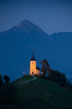 Geceleri Slovenya Alpleri 'ndeki Jamnik köyünde St. Primoz ve Felicijan Kilisesi' ni aydınlattı. Dikey görünüm