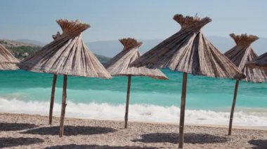 Hırvatistan 'ın Baska kentindeki Vela plajında Krk adasında saman şemsiyeler bulunuyor. Turkuaz Adriyatik Denizi ve kıyıya vuran dalgalar.