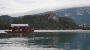 Slovenya 'da Kan Gölü. Turistli ahşap tekneler gölde yelken açıyor. Arka planda da da Bled Castle tepede..