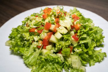 Yeşil marul yapraklı bir salata, taze soğan, kırmızı biber, salatalık ve tabakta bitki sosu.