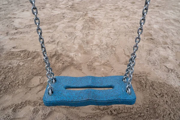 Blue empty swing with metal chain and sand floor in the background