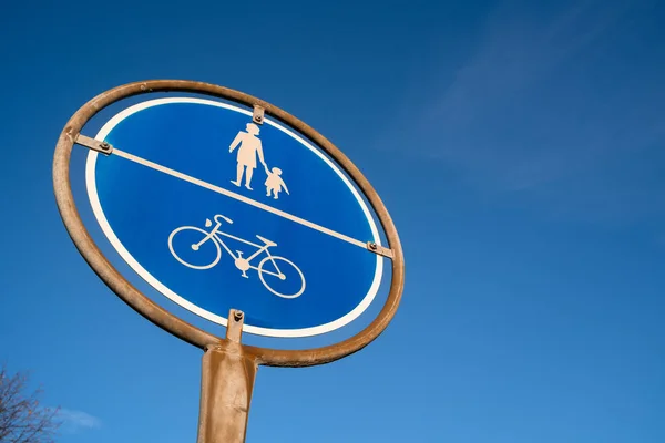 Blue circular sign for pedestrians and cyclists on a rusty post with blue sunny sky in the background
