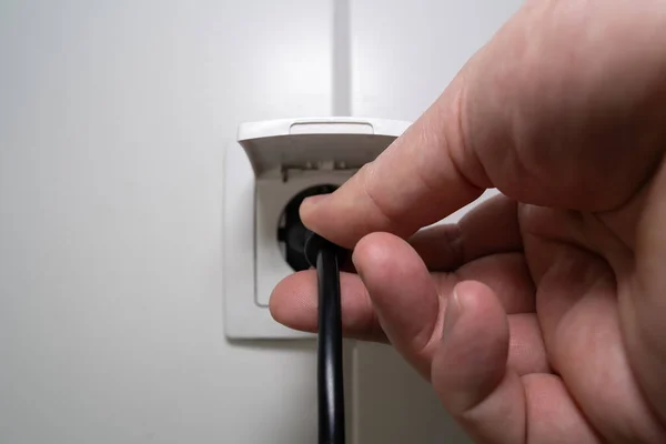 Male hand plugs a power cable into the socket