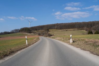 Kırsal kesimde yol, tarım arazileri, ağaçlar ve baharda mavi güneşli bir gökyüzü.