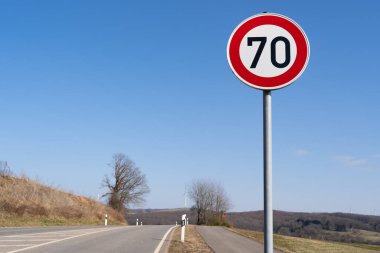 Mavi güneşli gökyüzü olan bir kır yolunda hız işareti saatte 70 kilometre 