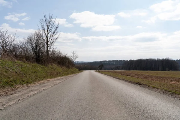 stock image Asphalt road in the landscape with leafless trees and a bright sky on a sunny day in spring