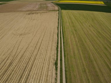 Tarım tarlaları ile baharda toprakla sürülmüş tarlalar arasındaki uzun toprak yolun üzerinden manzaraya bak. 
