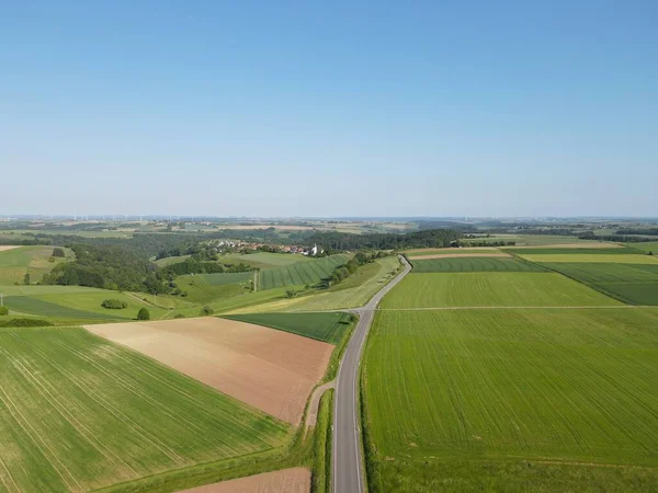 緑の畑が広がる風景の上からの眺め 真ん中にアスファルトの道 そして青空 — ストック写真