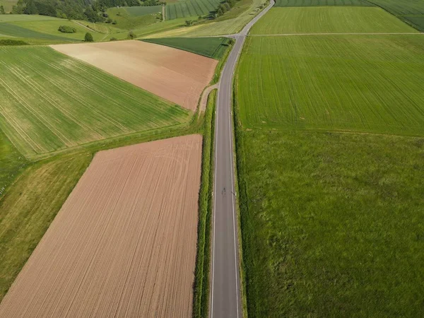 緑の農地と作物との間の長いアスファルトの道路や春には上記から地球を耕した — ストック写真