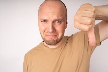 Genç adam üzgün surat yapıyor ve baş parmağını aşağı gösteriyor.