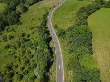 Çevredeki ağaçlar ve yeşil otlar arasında uzun, dolambaçlı asfalt bir yol. 