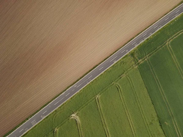 土壌と茶色の耕起農業分野と作物と緑の成長分野との間の風景の中にアスファルト道路の空中ビュー — ストック写真