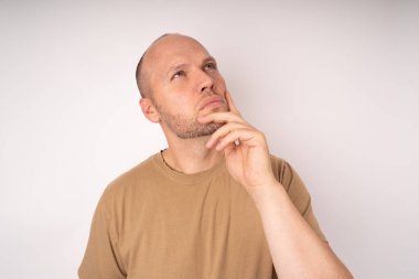 Kahverengi tişörtlü genç adam elini çenesine dayayıp iyi bir fikir ve iyi bir çözüm düşünüyor.