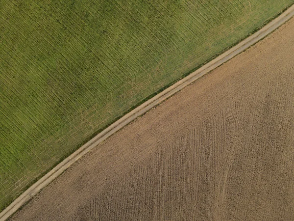 農地に汚れがある緑地と耕された畑の間の汚れた道の空中観察 — ストック写真