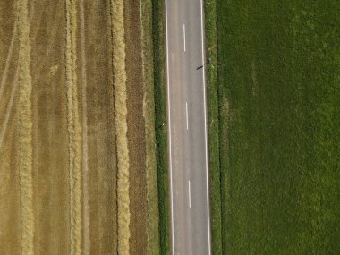 Çimenli saman tarlası ile yeşil çim tarlası arasındaki yolun havadan görünüşü 