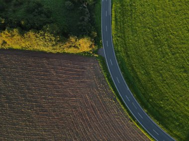 Çevredeki tarım alanları arasında uzanan eğimli bir yolun havadan görünüşü  