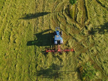 Çim tarlasında saman biçme makinesi olan bir traktörün hava görüntüsü.