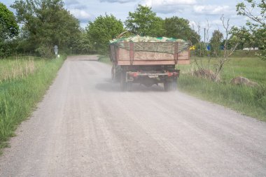 Tozlu bir çakıl yolunda içi odun dolu bir treyleri olan bir traktör.