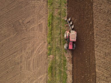 Kırmızı traktörün havadan görünüşü tarlayı sürüyor. 
