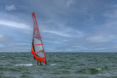 Okyanus sularındaki dinamik rüzgar sörfçüsü Bulutlu Mavi Gökyüzünün Altında