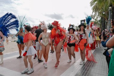 Sitges, İspanya - 8 Haziran 2025: İnsanlar Sitges Onur Yürüyüşü sırasında gökkuşağı bayrakları sallayarak renkli kıyafetler içinde sevinçle yürüyorlar. Kalabalık deniz kenarında aşkı, çeşitliliği ve LGBTQ + gururunu kutluyor.