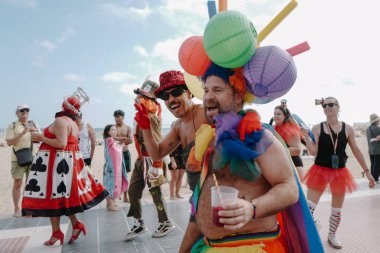 Sitges, İspanya - 8 Haziran 2025: İnsanlar Sitges Onur Yürüyüşü sırasında gökkuşağı bayrakları sallayarak renkli kıyafetler içinde sevinçle yürüyorlar. Kalabalık deniz kenarında aşkı, çeşitliliği ve LGBTQ + gururunu kutluyor.