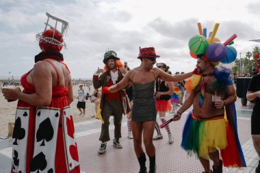 Sitges, İspanya - 8 Haziran 2025: İnsanlar Sitges Onur Yürüyüşü sırasında gökkuşağı bayrakları sallayarak renkli kıyafetler içinde sevinçle yürüyorlar. Kalabalık deniz kenarında aşkı, çeşitliliği ve LGBTQ + gururunu kutluyor.