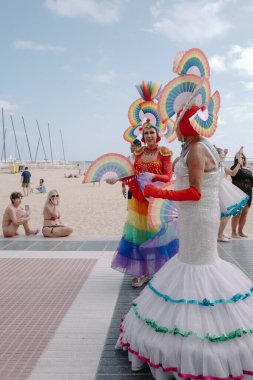 Sitges, İspanya - 8 Haziran 2025: İnsanlar Sitges Onur Yürüyüşü sırasında gökkuşağı bayrakları sallayarak renkli kıyafetler içinde sevinçle yürüyorlar. Kalabalık deniz kenarında aşkı, çeşitliliği ve LGBTQ + gururunu kutluyor.