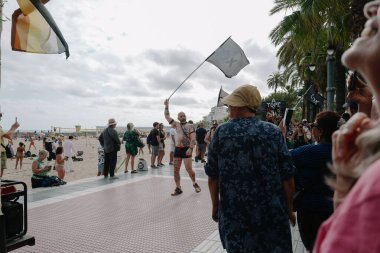 Sitges, İspanya - 8 Haziran 2025: İnsanlar Sitges Onur Yürüyüşü sırasında gökkuşağı bayrakları sallayarak renkli kıyafetler içinde sevinçle yürüyorlar. Kalabalık deniz kenarında aşkı, çeşitliliği ve LGBTQ + gururunu kutluyor.