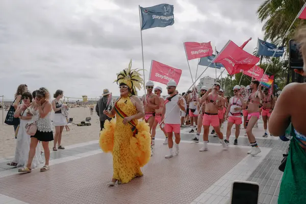 Sitges, İspanya - 8 Haziran 2025: İnsanlar Sitges Onur Yürüyüşü sırasında gökkuşağı bayrakları sallayarak renkli kıyafetler içinde sevinçle yürüyorlar. Kalabalık deniz kenarında aşkı, çeşitliliği ve LGBTQ + gururunu kutluyor.