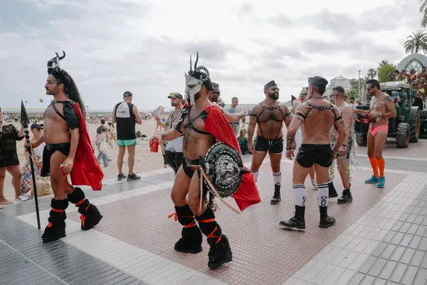 Sitges, İspanya - 8 Haziran 2025: İnsanlar Sitges Onur Yürüyüşü sırasında gökkuşağı bayrakları sallayarak renkli kıyafetler içinde sevinçle yürüyorlar. Kalabalık deniz kenarında aşkı, çeşitliliği ve LGBTQ + gururunu kutluyor.