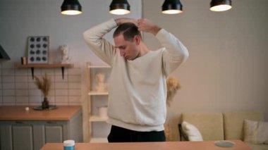 Young man ties his hair in a ponytail. Looks in the mirror then picks up face cream from the table and sniffs it.