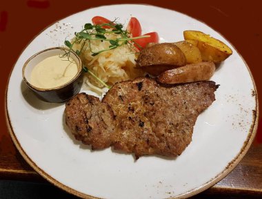 Büyük bir parça ızgara domuz eti ve beyaz tabakta ev yapımı patates..