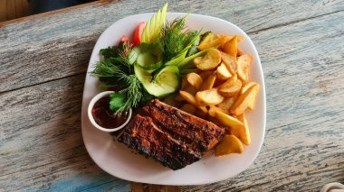 Piece of fried meat and homemade potatoes with sauce and fresh vegetable salad on white plate.