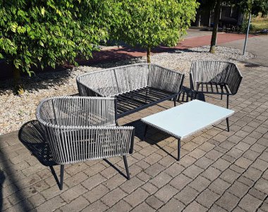 Woven armchairs and a small table are displayed on the cobblestones on a sunny day.