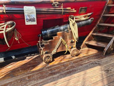 The ships cannon is secured with ropes on the deck of an old wooden sailboat.
