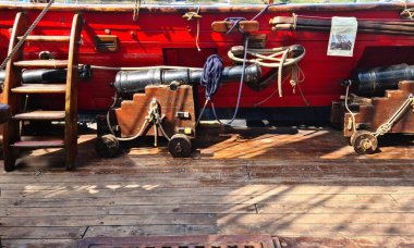 The ships cannon is secured with ropes on the deck of an old wooden sailboat.