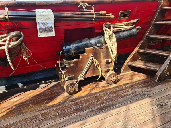 The ships cannon is secured with ropes on the deck of an old wooden sailboat.