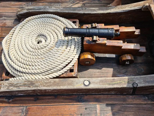 The ships cannon is secured with ropes on the deck of an old wooden sailboat.