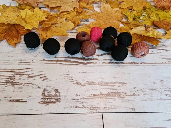 Knitting woolen threads in balls are scattered on table with yellow maple leaves.