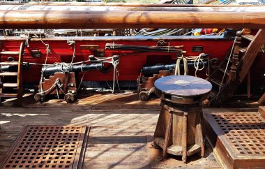 Wooden windlass and black cannons along the side of an old sailing ship.