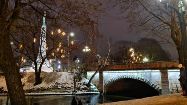 Özgürlük Anıtı ve taş köprü 2022 kışında Letonya 'nın başkenti Riga' daki spot ışıklarıyla aydınlandı..