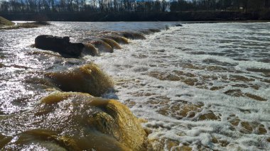Baharın erken saatlerinde güneşli bir günde geniş nehir boyunca küçük bir şelale..