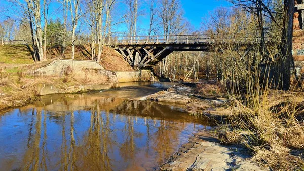 An old small bridge across narrow stream on sunny spring day.