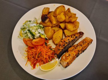 İki parça kızarmış balık, patates ve tabakta taze salata..