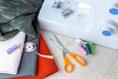 Kumaş, makas, dikiş makinesi ve ahşap bir masa üzerine çeşitli dikiş malzemeleri.